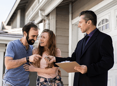A real estate professional speaking with a couple outside a home